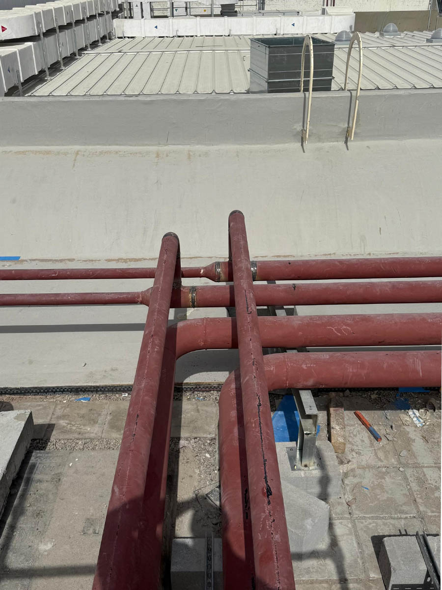 Red-coated steel pipework running across a building rooftop