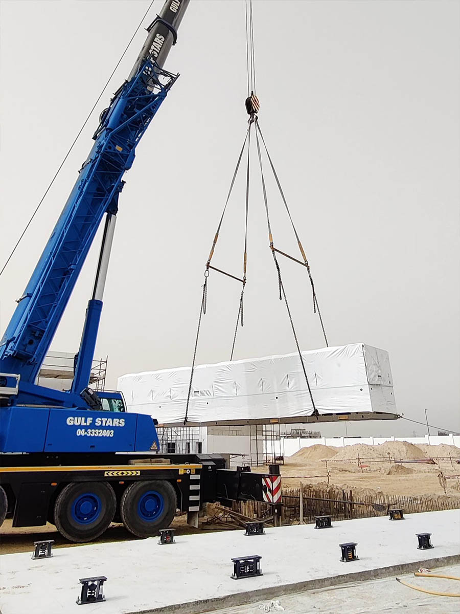 Crane hoisting a large rectangular plant unit into position on site
