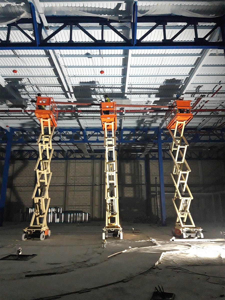 Three scissor lifts raising a red pipe section to roof level