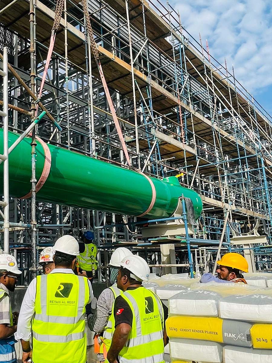 Crane lifting a large green-coated pipe section into position